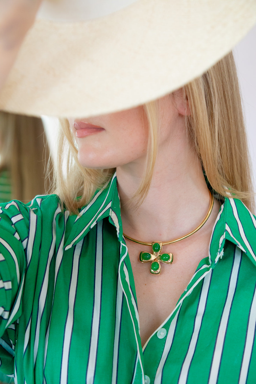 Gold necklace with green gemstones worn by a person in a green and white striped shirt. Palm Beach based jewelry designers Pelimingo Palm Beach made in 14K or 18K yellow gold cross or pendant or clover