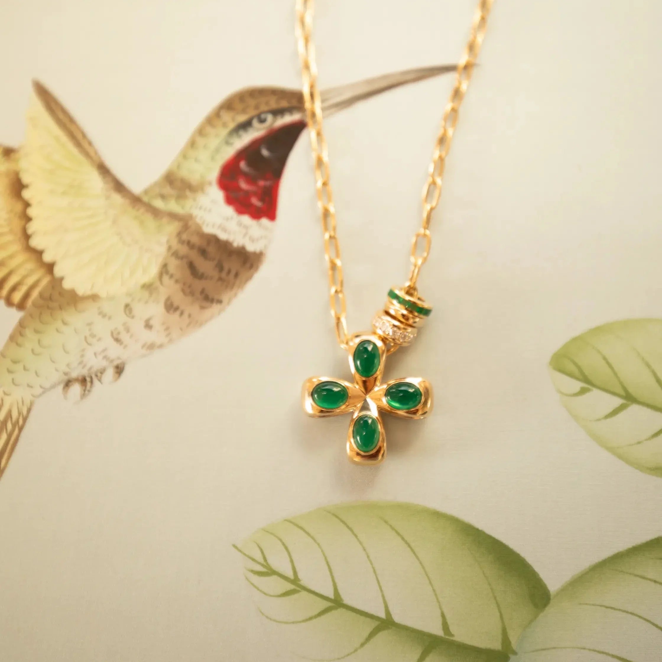 Gold necklace with green gemstones worn by a person in a green and white striped shirt. Palm Beach based jewelry designers Pelimingo Palm Beach made in 14K or 18K yellow gold cross or pendant or clover
