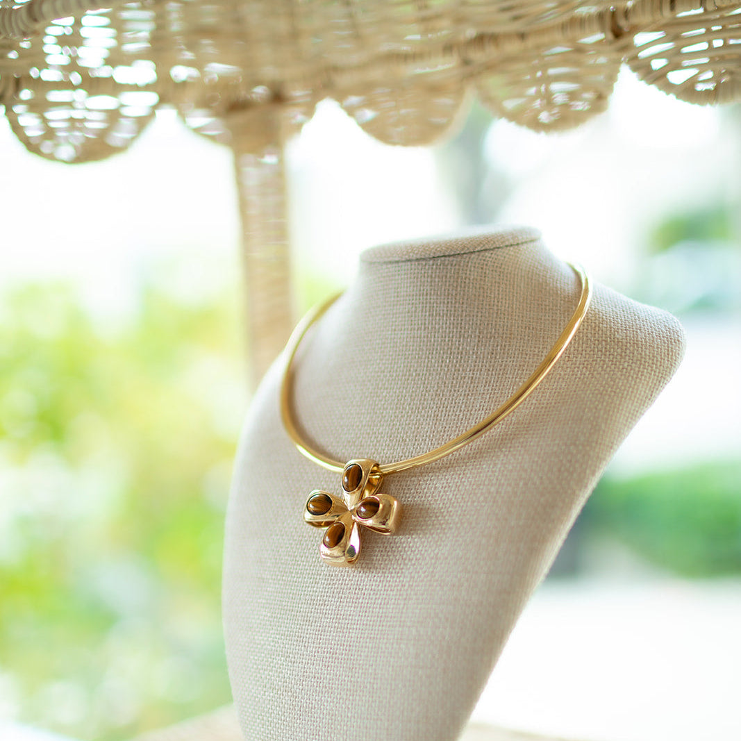 Gold necklace on a mannequin bust with a blurred natural background.  On a gold collar is our Tiger Eye clover/cross in 14K gold