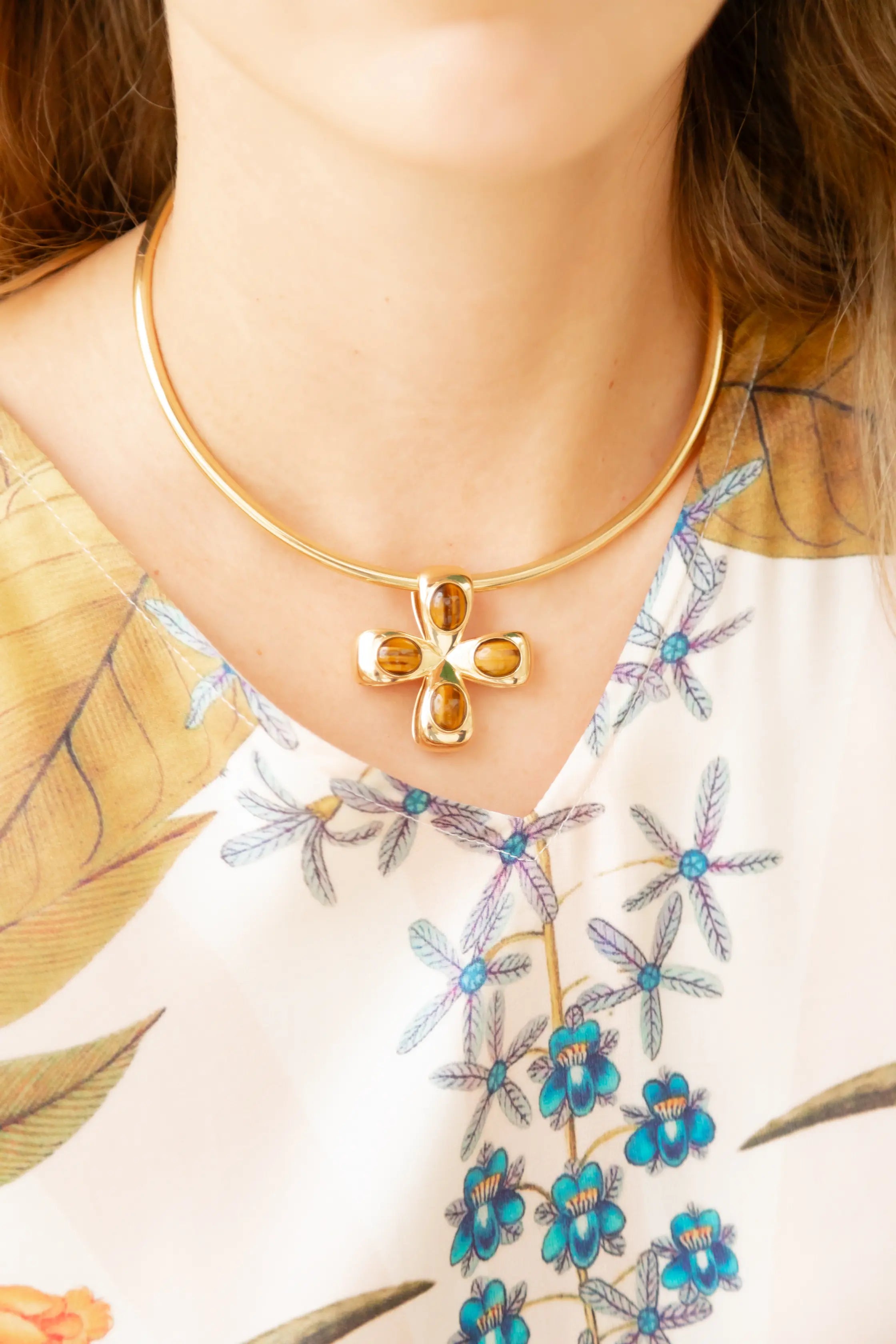 Gold necklace with a cross pendant worn by a person against a floral background.  The 14K or 18K Large Cross glider called the Everglades Glider is a beautiful charm for any necklace or collar.  Palm Beach based Jewlery designers Pelimingo Palm Beach