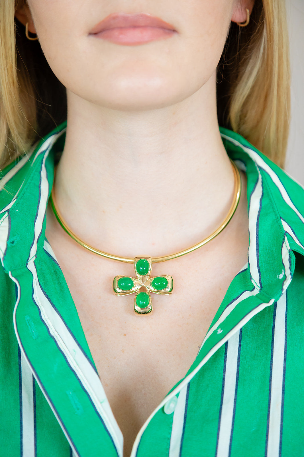 Gold necklace with green gemstones worn by a person in a green and white striped shirt. Palm Beach based jewelry designers Pelimingo Palm Beach made in 14K or 18K yellow gold cross or pendant or clover