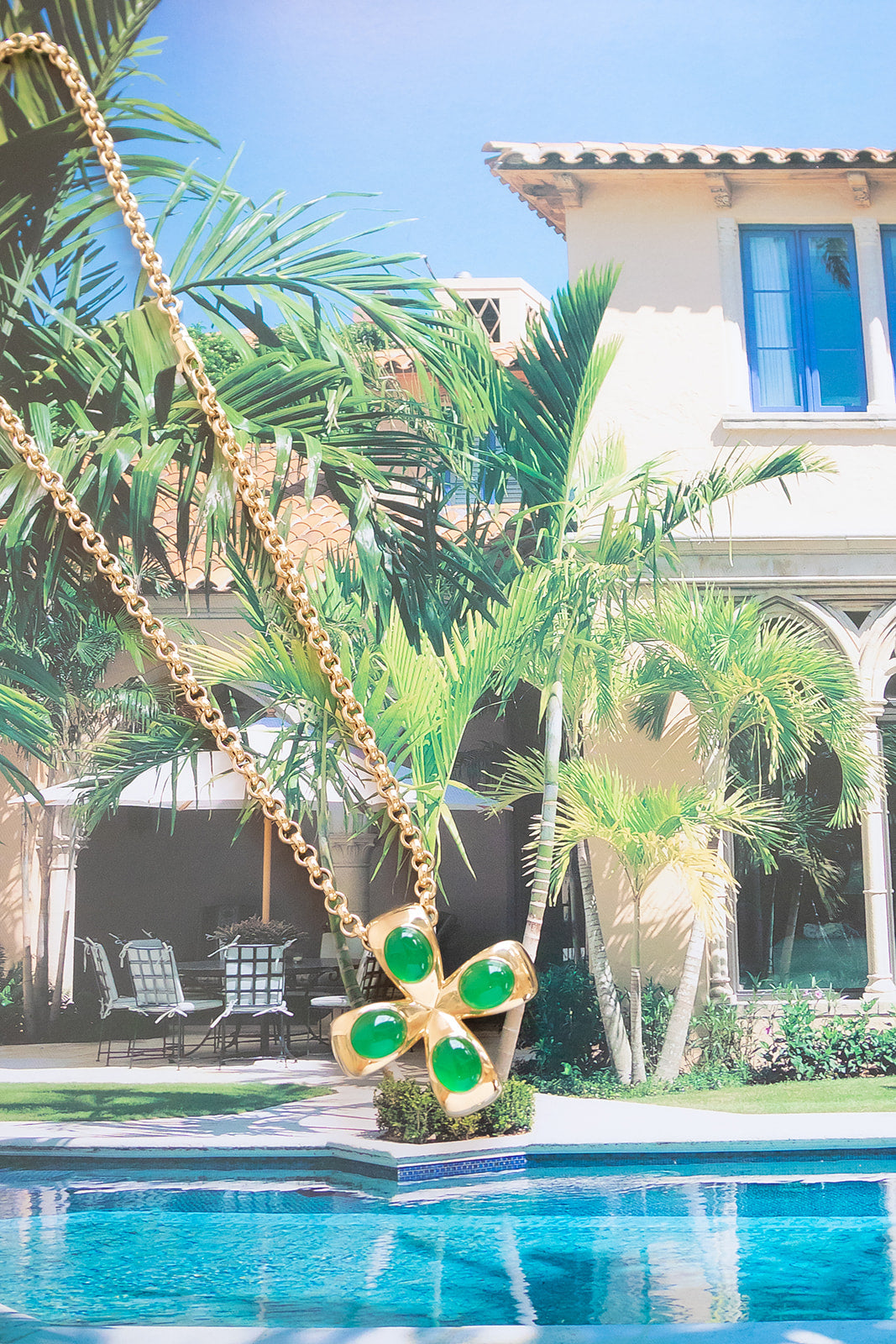 Gold necklace with green gemstones worn by a person in a green and white striped shirt. Palm Beach based jewelry designers Pelimingo Palm Beach made in 14K or 18K yellow gold cross or pendant or clover