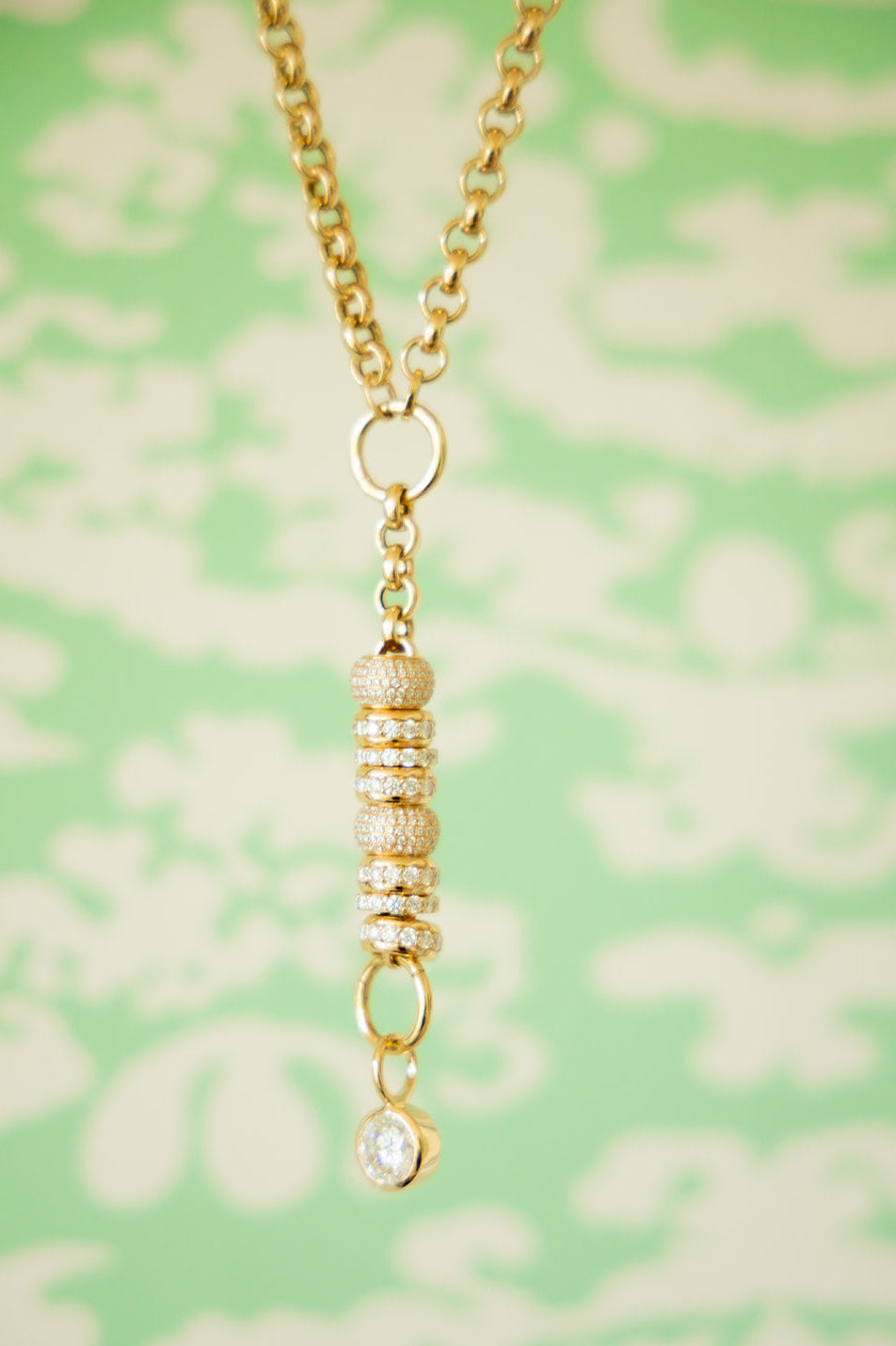 Gold necklace with a pendant on a green floral patterned background