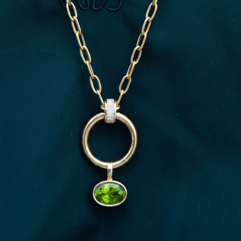 Gold pendant with a green gemstone on a white background, light green peridot set in 14K yellow gold.  Made by design team in Palm Beach, Florida Pelimingo Palm Beach.  Worn on necklace or collar