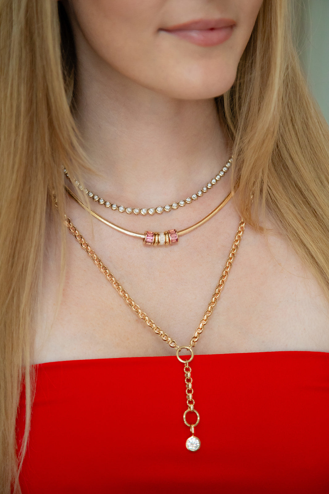 Close-up of a person wearing multiple gold necklaces with a red top.