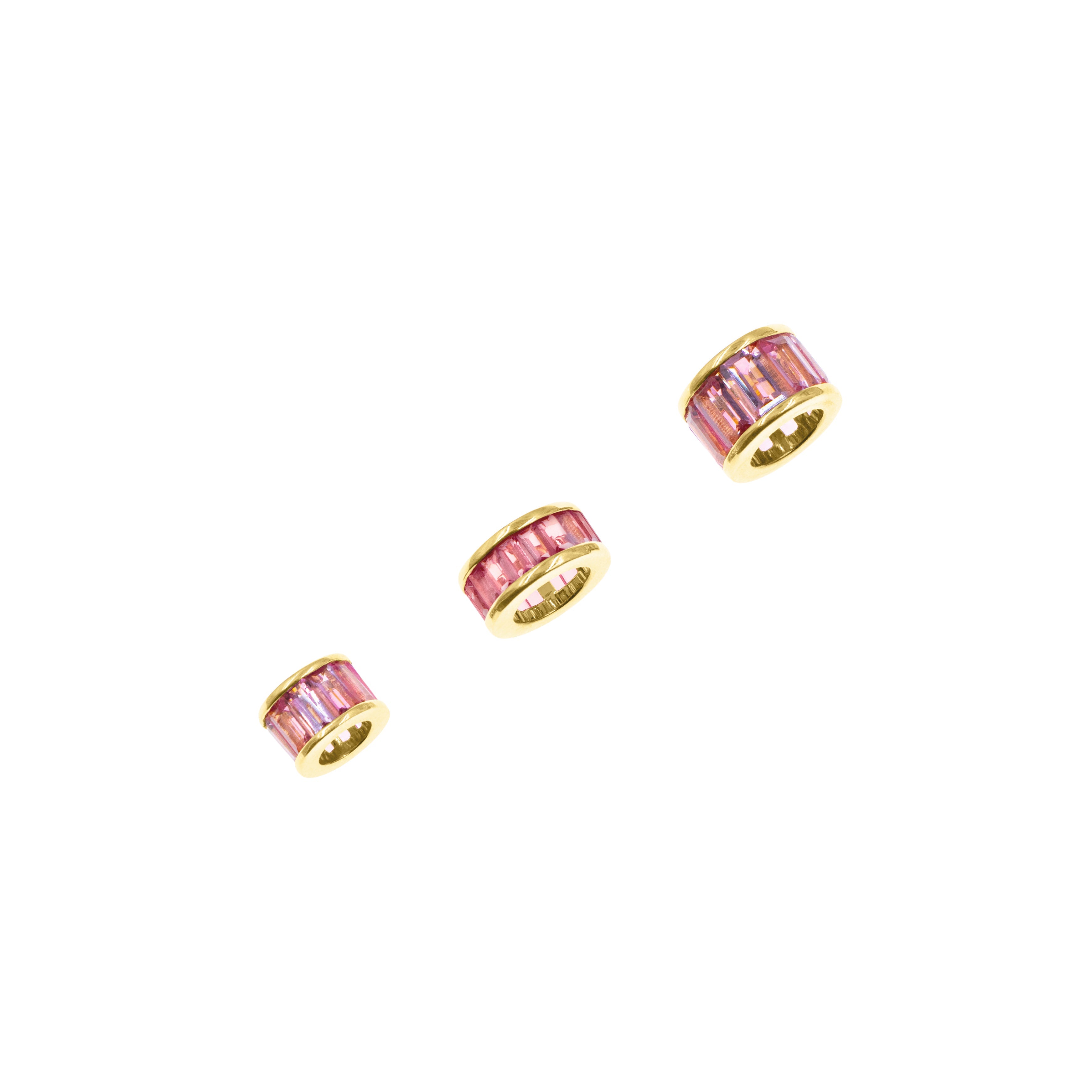 Three gold-toned cylindrical jewelry charms with pink gemstone accents, arranged diagonally on a plain white background.