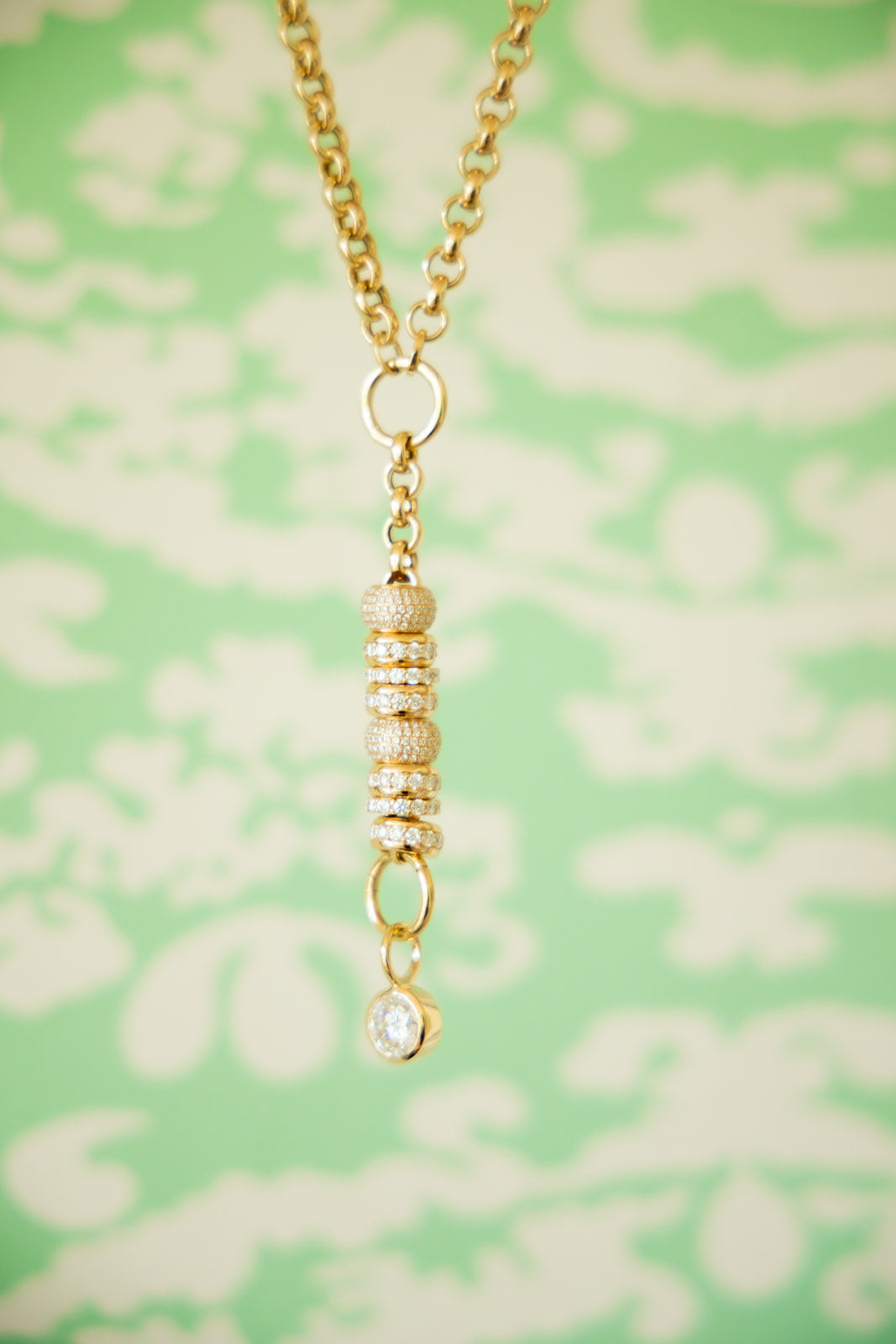 Gold necklace with a pendant on a green floral patterned background