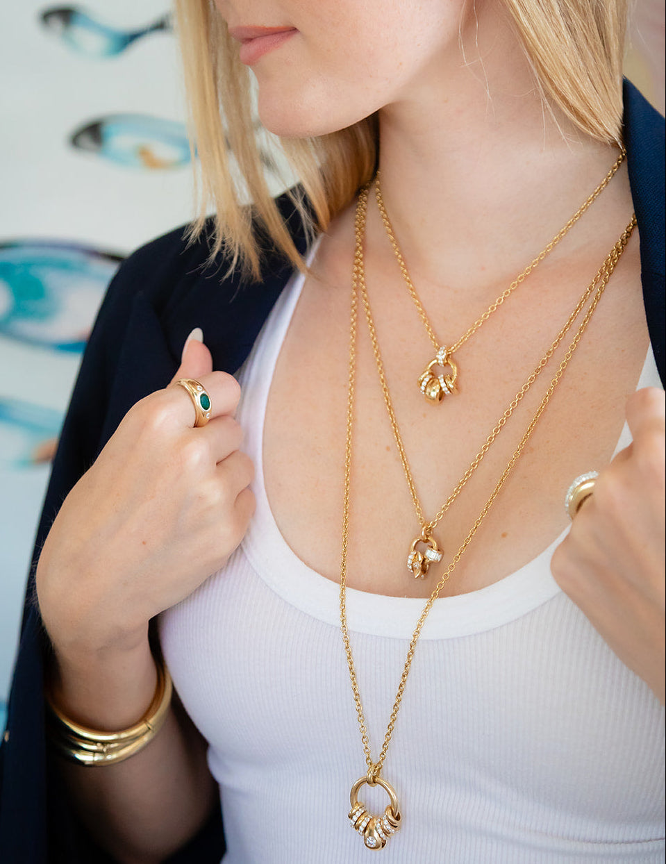 Woman wearing gold necklaces and a ring, with a colorful fish mural in the background, Palm Beach Chic Jewlery, designers