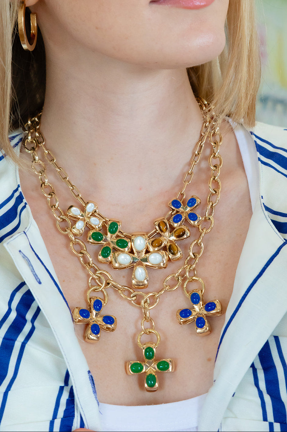 Gold necklace with green gemstones worn by a person in a green and white striped shirt. Palm Beach based jewelry designers Pelimingo Palm Beach made in 14K or 18K yellow gold cross or pendant or clover