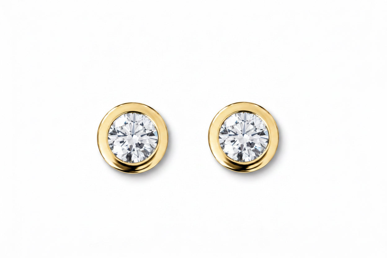 A pair of round gold stud earrings with clear round-cut gemstones, set against a plain white background. 14k yellow gold thick gold bezel with lab diamonds.  Made and designed by Pelimingo Palm Beach Fine jewelry.  Local jewelry brand.  